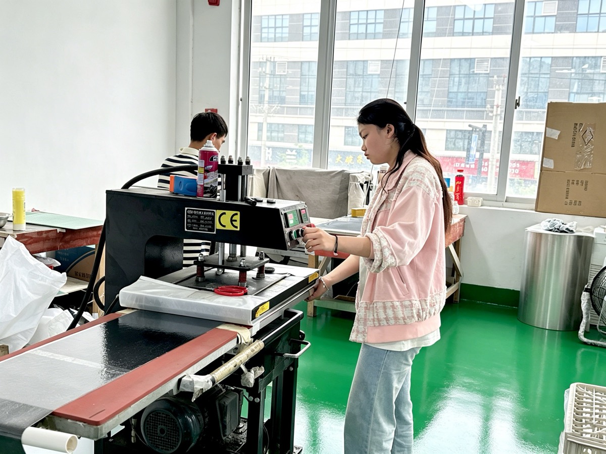 Heat press station at the LOCACRYSTAL Pujiang factory — operator running a rhinestone transfer press