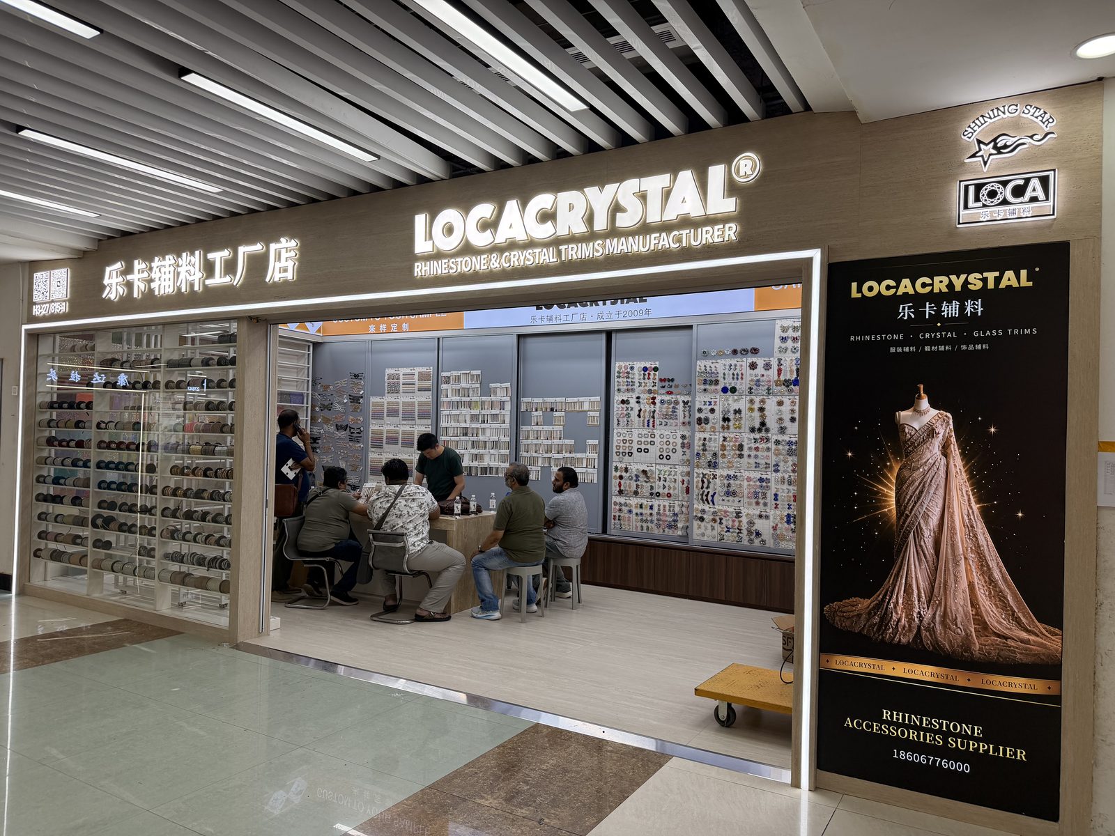 LOCACRYSTAL Yiwu showroom storefront — Booth 27815-1, Floor 3, Zone H, Yiwu International Trade City, rhinestone and crystal trims sample wall inside